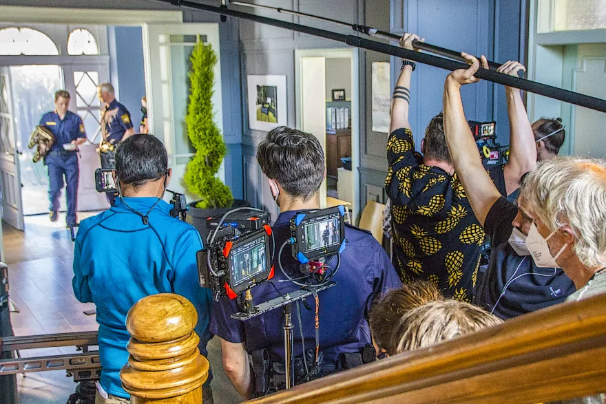 Drehtag am Set: Kamerateam, Tonangel und Darsteller in Polizeiuniform im Treppenhaus