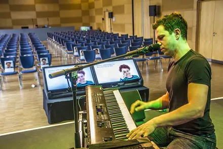 Nepo Fitz beim Soundcheck am Klavier, dahinter ein großer Saal mit leeren Stuhlreihen