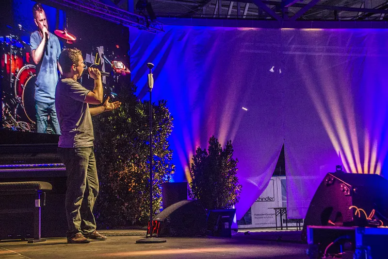 Nepo Fitz singt auf der Bühne, links die Leinwand mit seinem Livebild